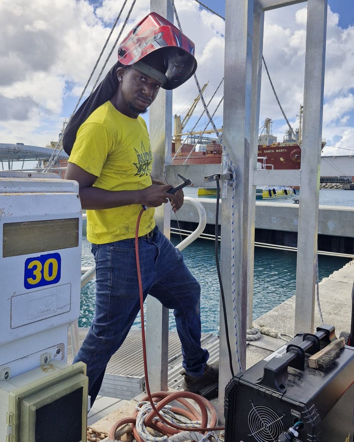 Kris on a marina dock with his TIG torch, beside the aluminum frame he is welding